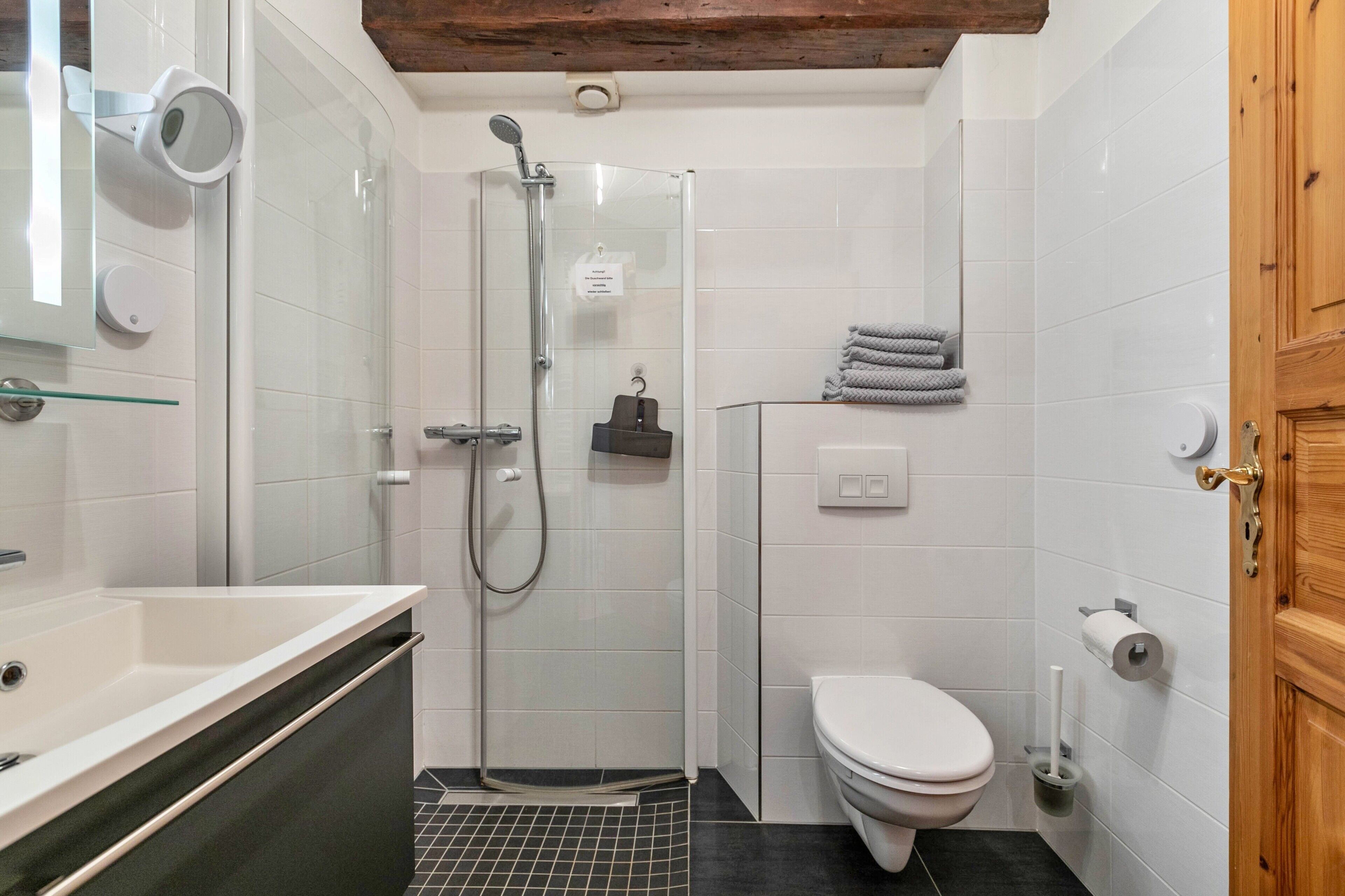 A modern bathroom with a glass-enclosed shower, a white toilet, and a sink with a mirror.
