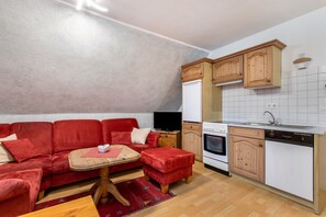 A compact living space with a red sofa, a small wooden table, a kitchen area with wooden cabinets and white appliances.