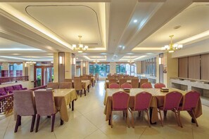 A spacious dining area with multiple tables and chairs, high ceilings with chandeliers, and large windows allowing natural light. - Mitin Holiday Hotel (Tengchong)