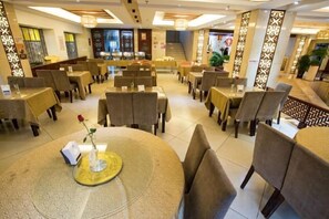 A restaurant with round tables and chairs, a staircase in the background, and decorative wall panels. - Mitin Holiday Hotel (Tengchong)
