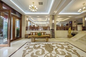 A hotel lobby with a large wooden bench, a patterned carpet, and a reception desk. - Mitin Holiday Hotel (Tengchong)
