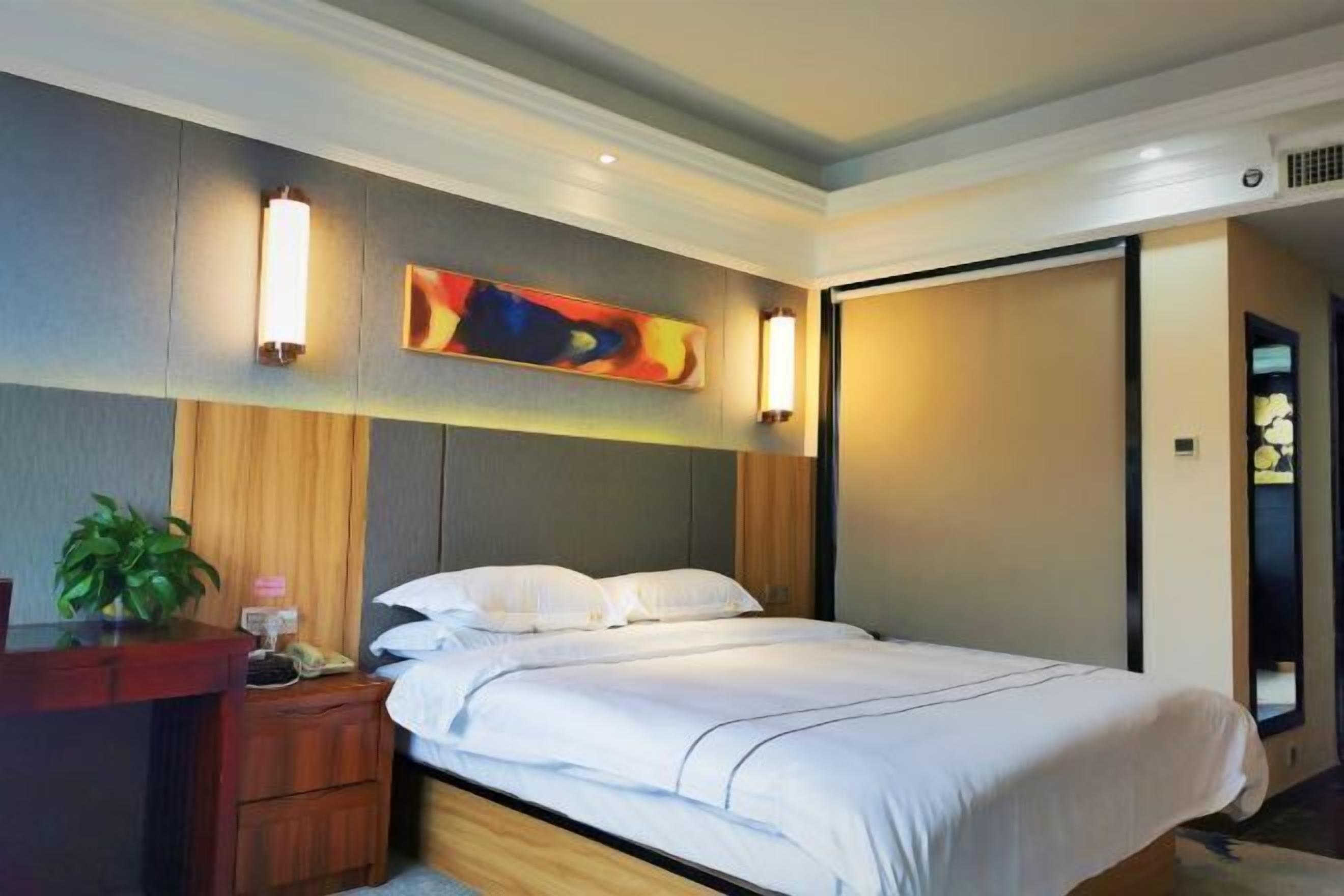 A hotel room with a bed, bedside tables, a desk, and a wall-mounted artwork.