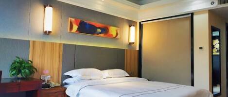 A hotel room with a bed, bedside tables, a desk, and a wall-mounted artwork.