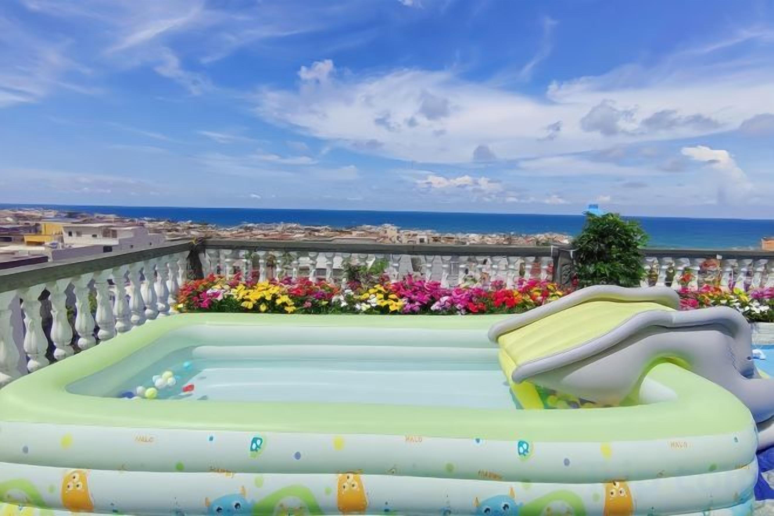Ein aufblasbarer Pool mit Rutsche auf einem Balkon mit Blick auf eine Stadtlandschaft und das Meer.