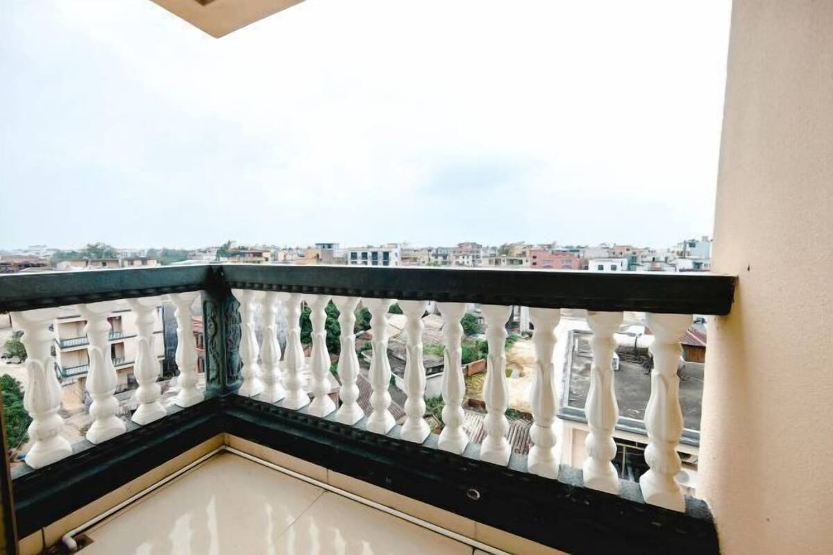 A balcony with a black balustrade and white balusters, overlooking a residential area with buildings and greenery.