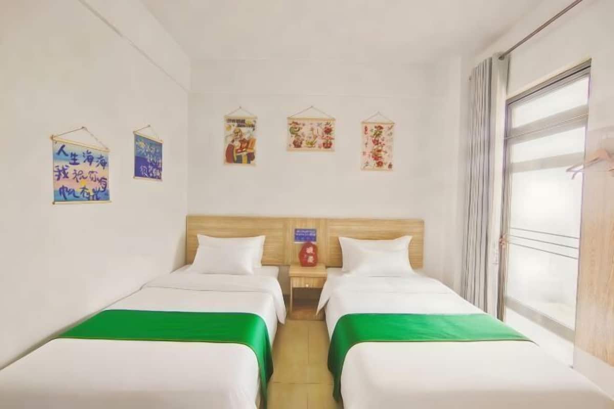 A hotel room with two beds, a wooden headboard, a window with curtains, and wall decorations.