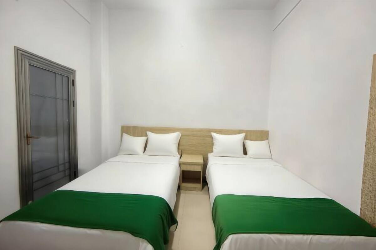 A small, clean room with two single beds, a wooden headboard, and a door with a glass panel.