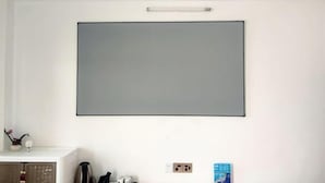 A room with a large, blank wall-mounted TV, a white cabinet with a decorative item, and a small table with a book and a kettle. - Beihai Fishing Village Inn (Silver Beach Tourist Resort) (Beihai)