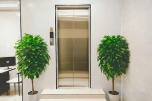 An elevator with a modern design, flanked by two potted plants. - Beihai Fishing Village Inn (Silver Beach Tourist Resort) (Beihai)