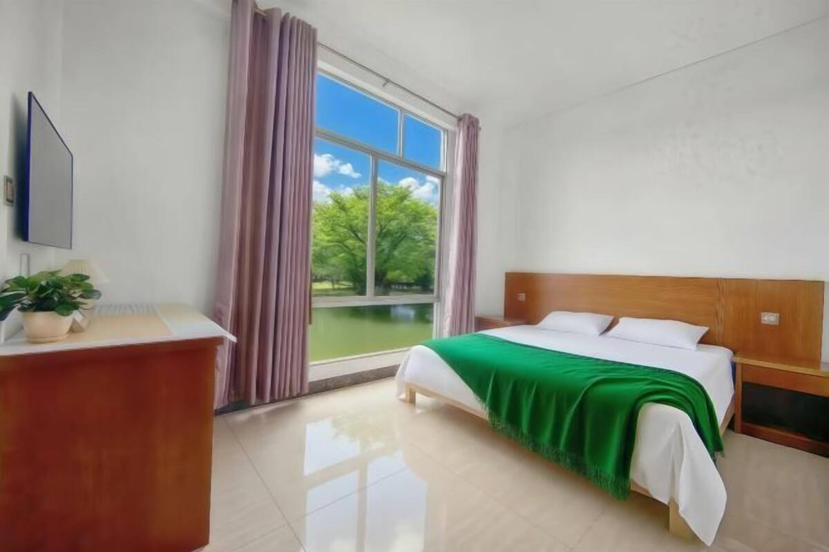 A hotel room with a bed, a desk, a TV, and a window with curtains.