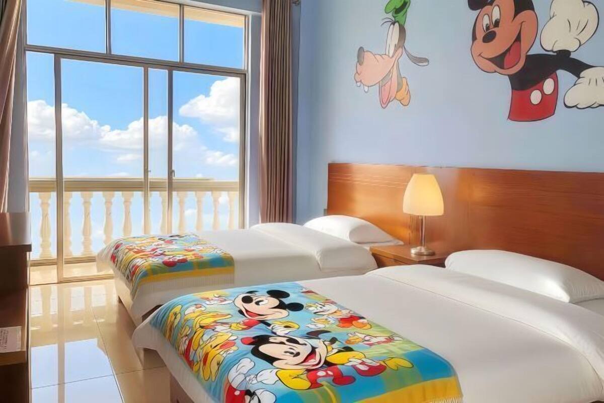 A hotel room with two beds, a balcony, and Mickey Mouse-themed bedding.
