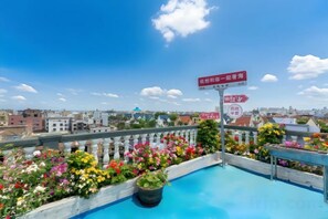 Une piscine sur le toit, offrant une vue sur la ville, entourée de fleurs et agrémentée d’un panneau indicateur.