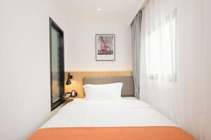 Habitación de hotel con cama, mesita de noche, un cuadro enmarcado en la pared y una ventana con cortinas.