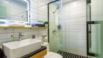 A modern bathroom with a large white sink, a toilet, a glass-enclosed shower, and a mirror above the sink.