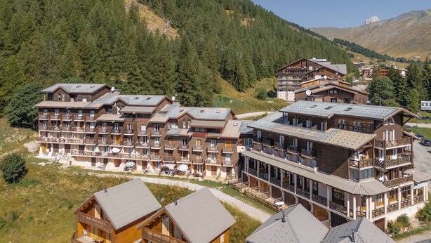 A mountain lodge with multiple wooden buildings, balconies, and a view of a forested mountain. - Magnificent 4-pers studio with fireplace (Allos)