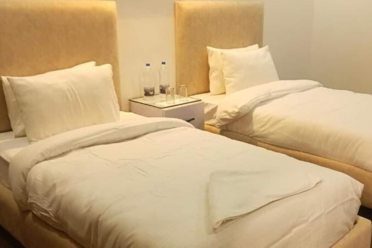 Ein Hotelzimmer mit zwei Einzelbetten, einem Nachttisch mit Lampe und einem kleinen Tisch mit zwei Flaschen.