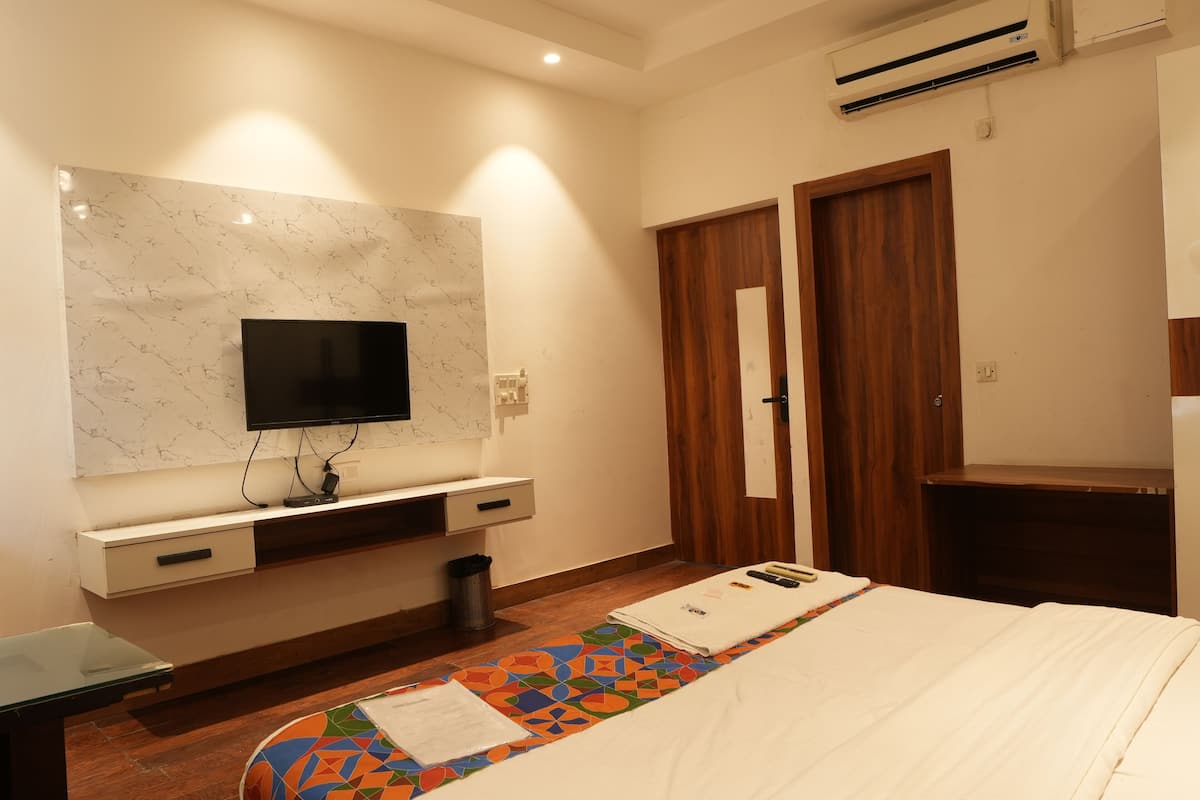 Ein Hotelzimmer mit Flachbildfernseher an einer Marmorwand, Holzschrank und einem Bett mit farbigem, geometrisch gemustertem Bettüberzug.