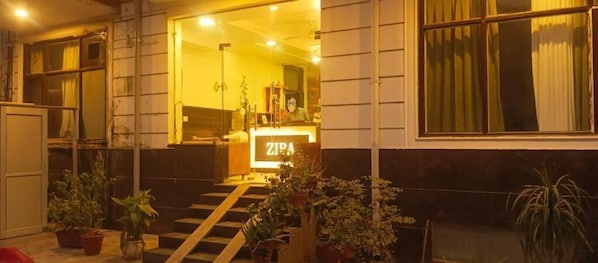 A hotel entrance with a reception desk labeled "ZIRA" and a staircase leading to the entrance.