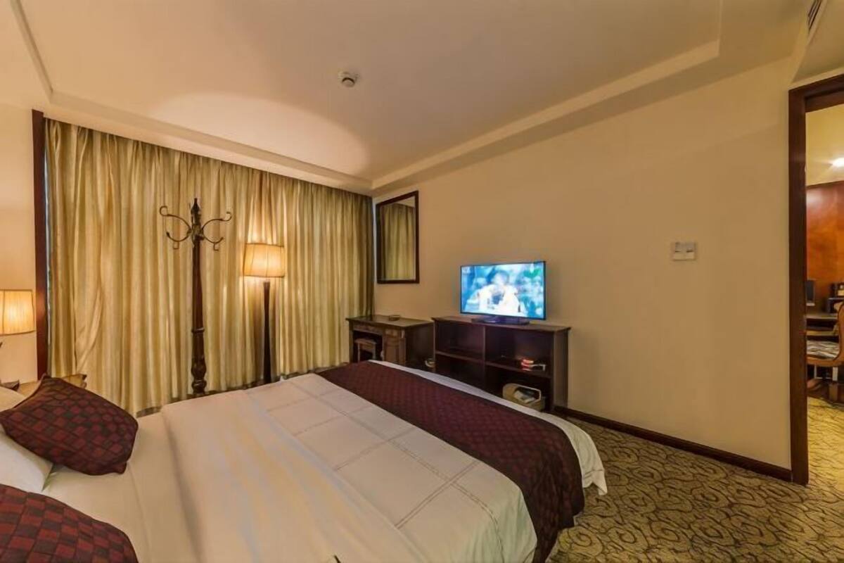 A hotel room with a large bed, a television, a desk with a lamp, and a mirror on the wall.