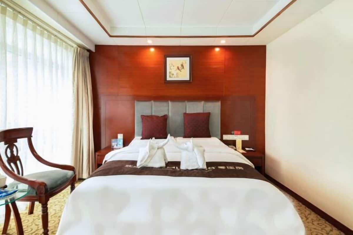 A hotel room with a bed, a chair, a nightstand, and a window with curtains.