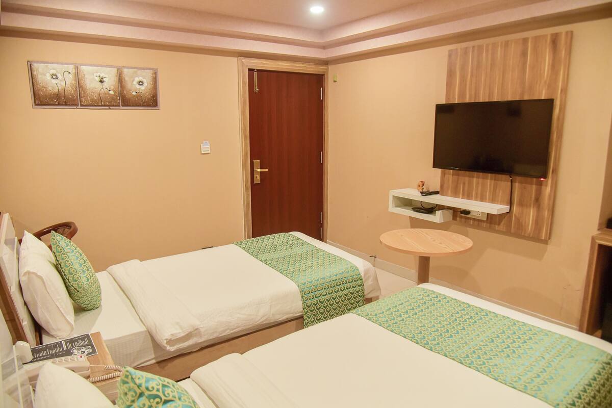 A hotel room with two beds, a TV mounted on the wall, a small round table, and a door.