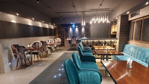 A modern restaurant interior with teal upholstered chairs, wooden tables, and a central bar area. - Hotel Apollo Grand (Guwahati)