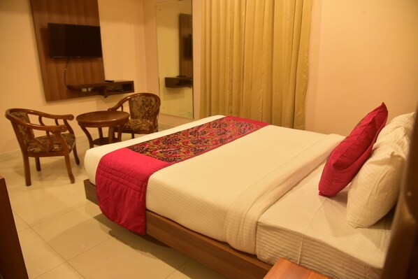 A hotel room with a bed, a TV mounted on the wall, a small table, two chairs, and a window with curtains. - Hotel Apollo Grand (Guwahati)