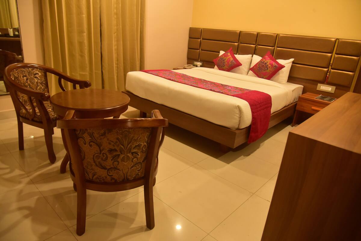 A hotel room with a bed, a bedside table, a chair, and a small round table.
