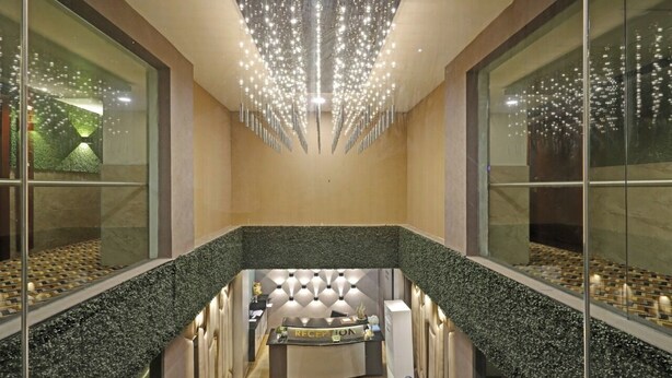 A modern reception area with a central desk, glass walls, and a unique chandelier design. - Hotel Apollo Grand (Guwahati)