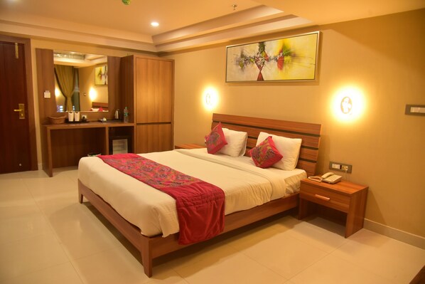 A well-lit bedroom with a large bed, bedside tables, a mirror, and a painting on the wall. - Hotel Apollo Grand (Guwahati)