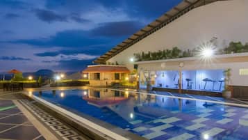 A swimming pool with a tiled deck, a covered area with exercise equipment, and a building with a curved roof.