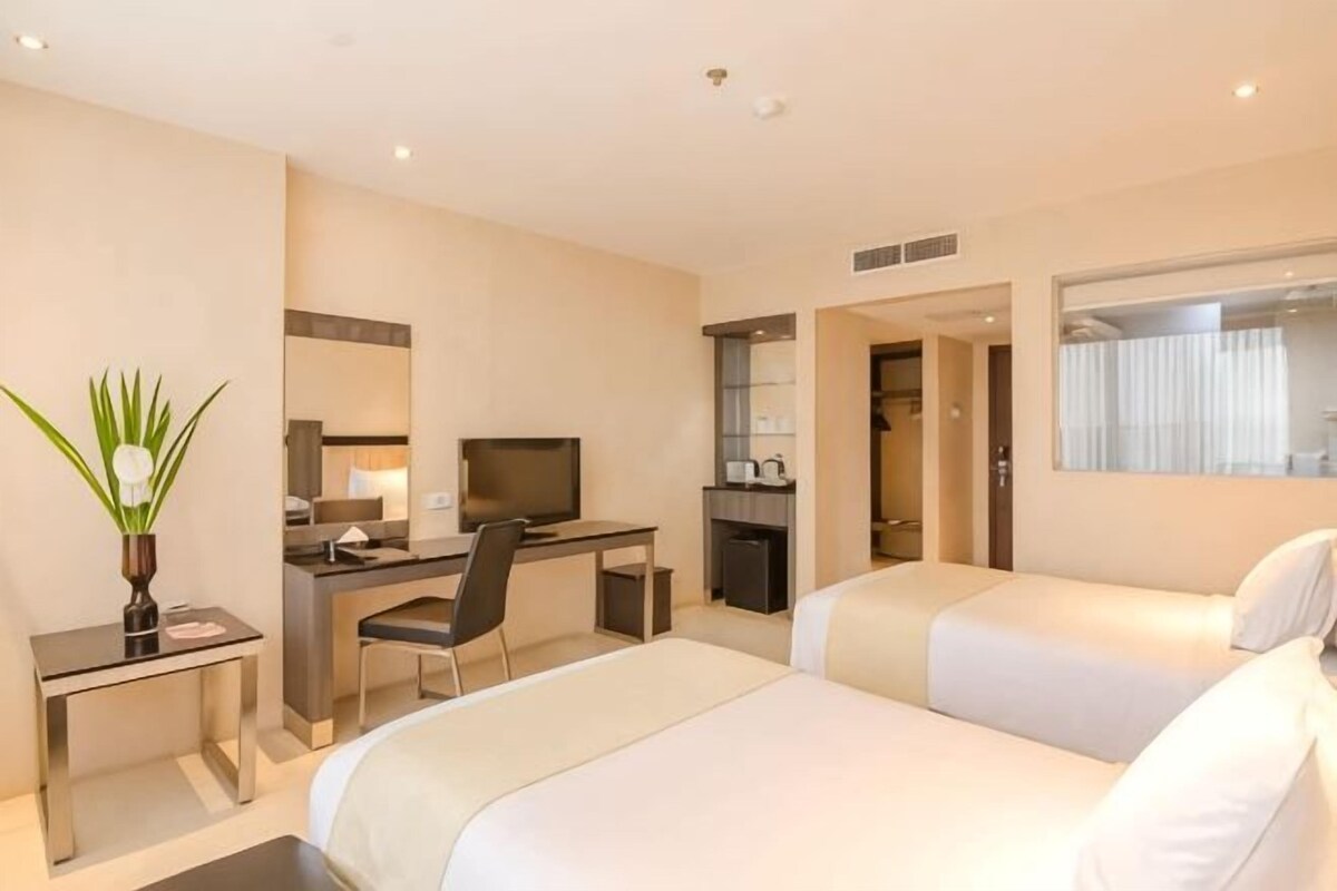 A hotel room with two beds, a desk with a chair, a television, and a bathroom visible through an open door.