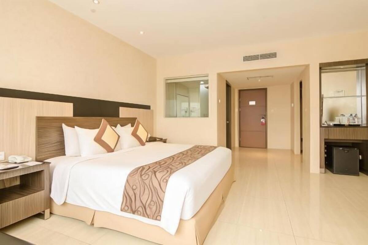 A hotel room with a large bed, a bedside table, a wardrobe, and a bathroom visible through an open door.