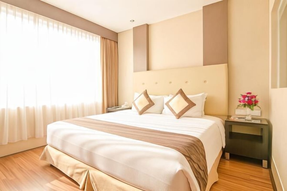 A hotel room with a large bed, a nightstand, a window with curtains, and a wall-mounted light fixture.