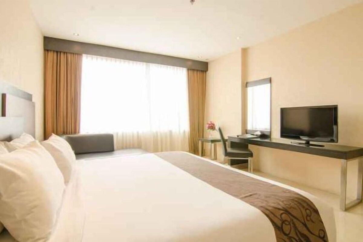 A hotel room with a bed, a desk, a television, and a window with curtains.
