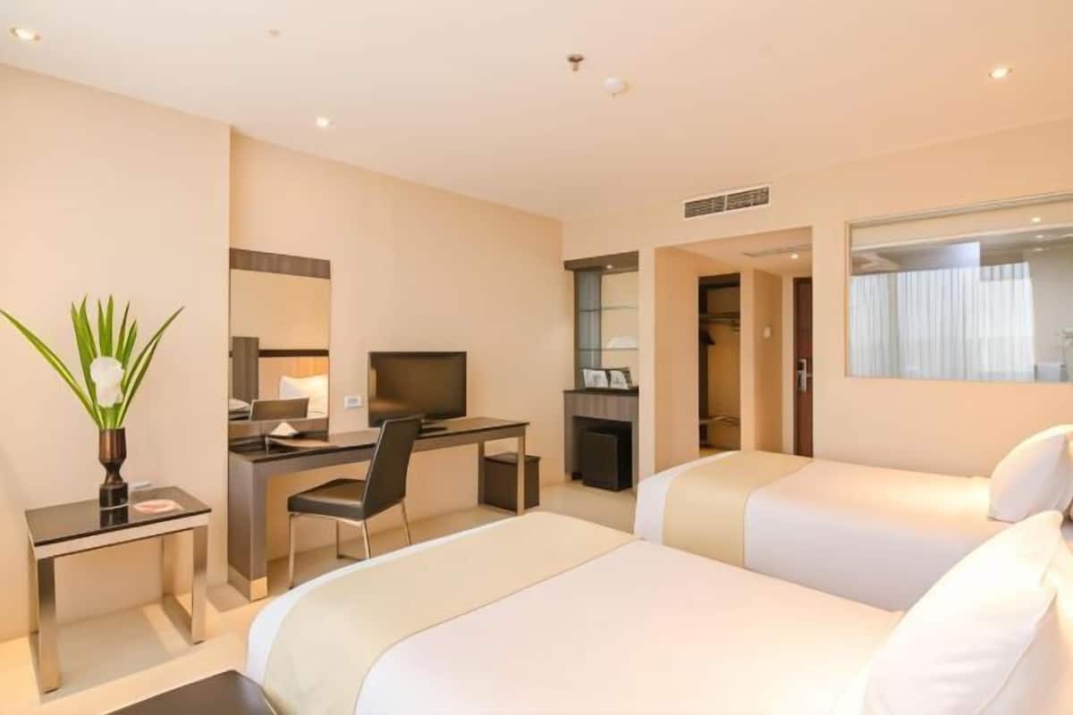 A hotel room with two beds, a desk, a chair, a TV, and a large window.