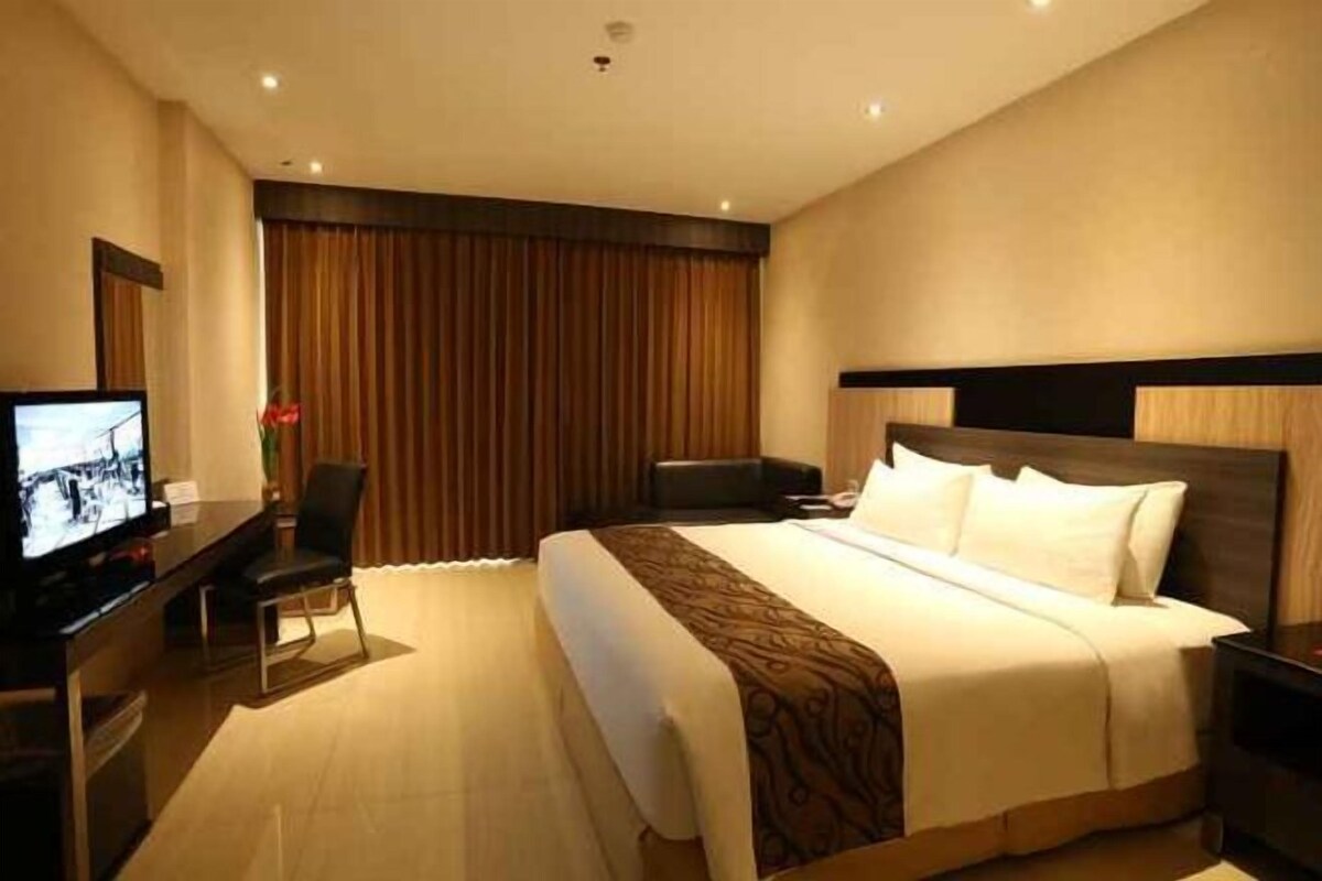 A hotel room with a large bed, a desk, a television, and a view of the outdoors.