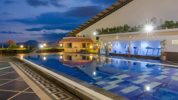 A swimming pool with a geometric tile pattern, a covered area with exercise equipment, and a building with a red roof in the background.