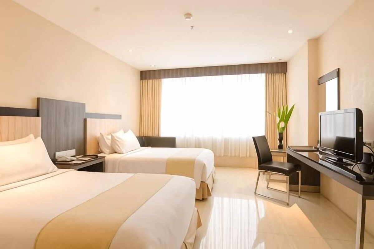A hotel room with two beds, a desk, a chair, and a television.