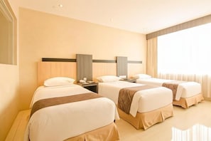 Three single beds with white duvets and brown throw blankets, set against a dark headboard.