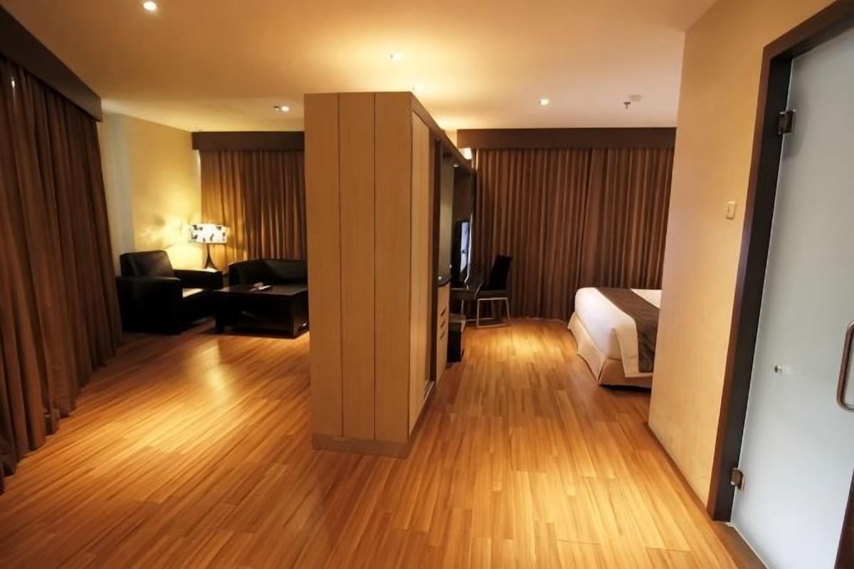 A hotel room with a wooden floor, a bed, a desk, and a chair.