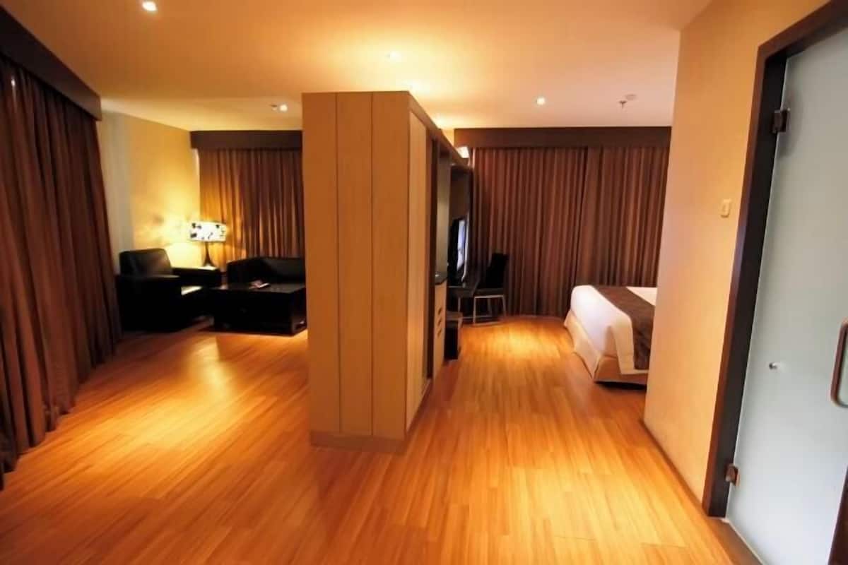A hotel room with a wooden floor, a bed, a desk with a chair, a TV, and a lamp.