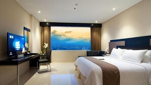 A modern hotel room with a large bed, a desk with a computer, a TV, and a view of the cityscape.