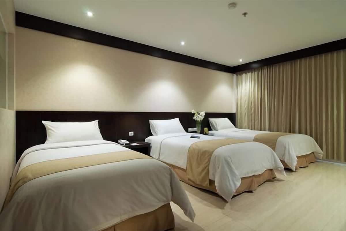 A hotel room with three beds arranged in a row, a nightstand between the beds, and a large window with curtains.