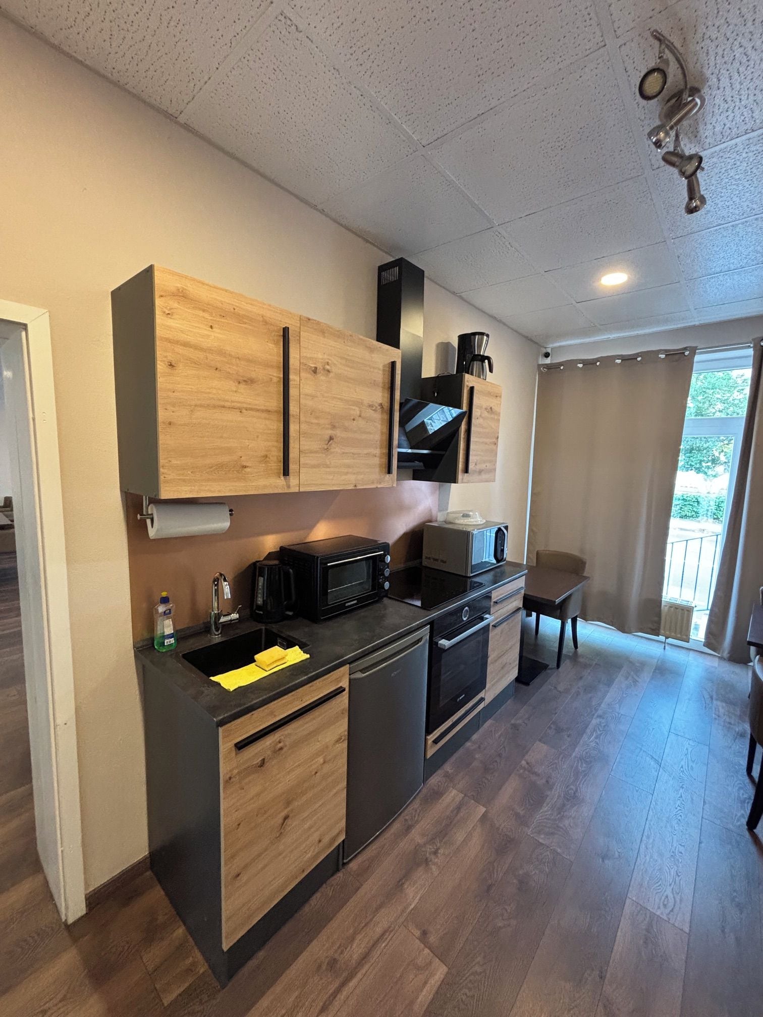 A compact kitchen with wooden cabinets, a microwave, a coffee maker, and a sink.