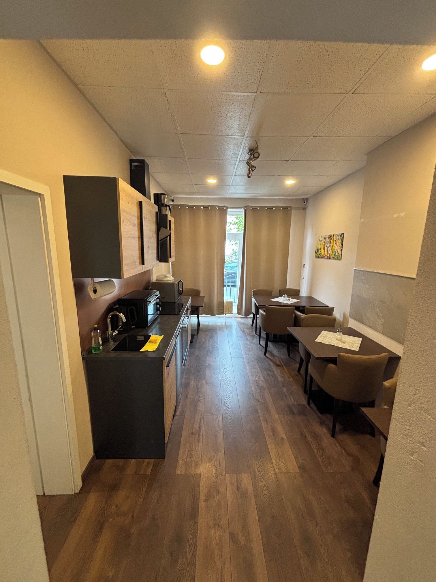 A compact hotel room with a kitchenette, a dining area with a table and chairs, and a large window providing natural light.