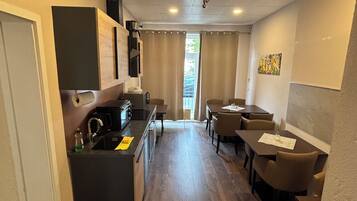 A compact hotel room with a kitchenette, a dining area with a table and chairs, and a large window providing natural light.