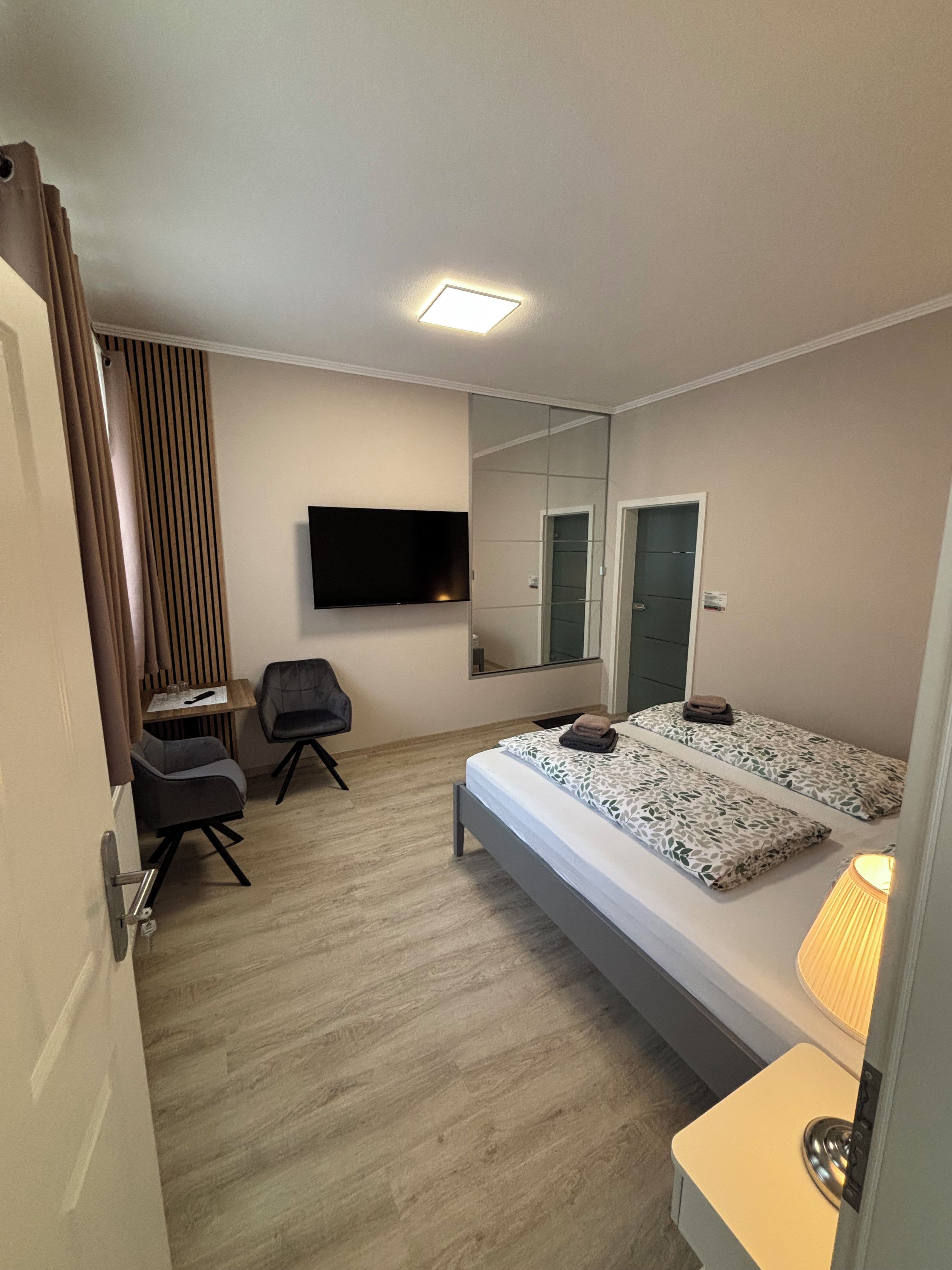 Ein Hotelzimmer mit Bett, Schreibtisch, Stuhl, Fernseher und Spiegel.