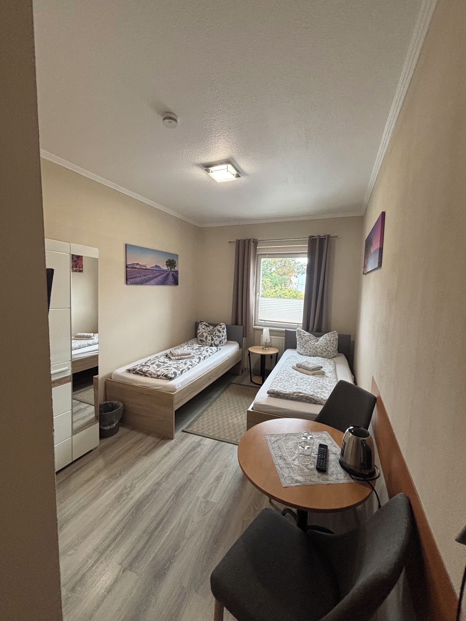 Une chambre d’hôtel de taille réduite, comprenant un lit simple, une petite table avec une chaise, un bureau et une fenêtre avec des rideaux.