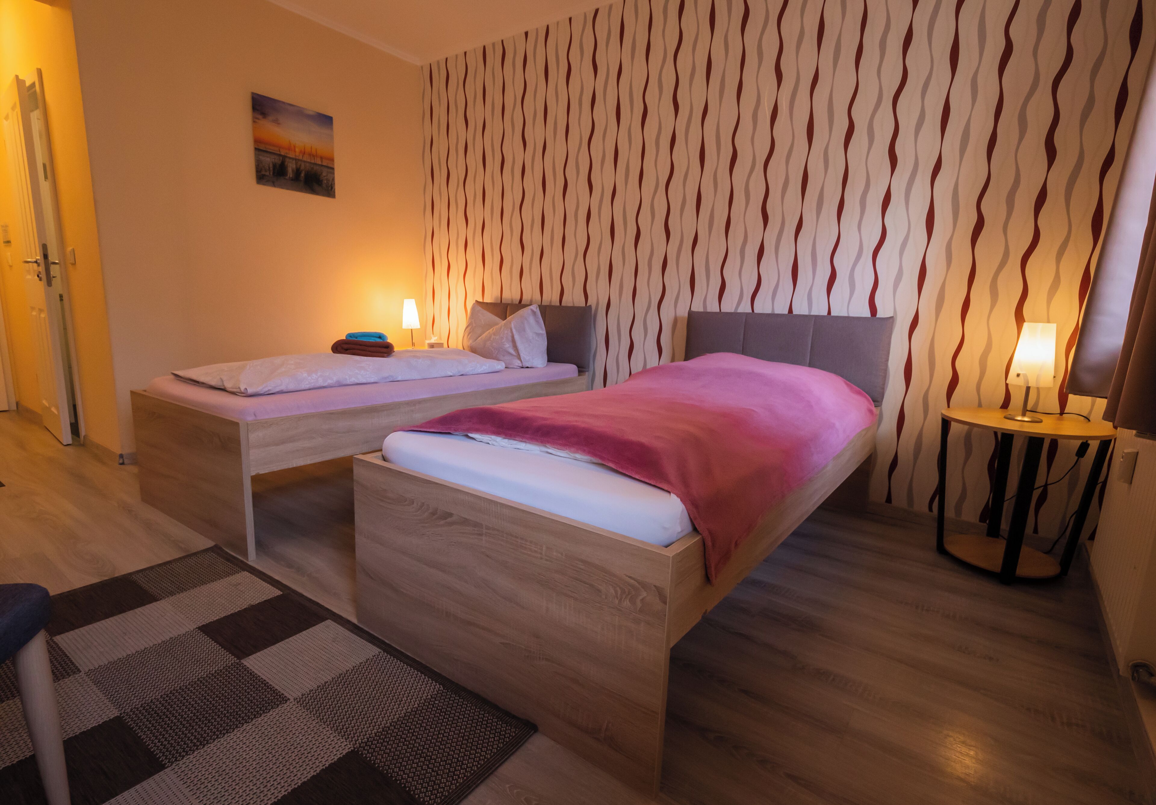 Een hotelkamer met twee bedden, behang met een patroon en een klein tafeltje met een lamp.
